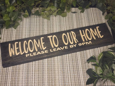 Welcome to Our Home. Please Leave by 9PM wood sign for humorous entryway wall art.
