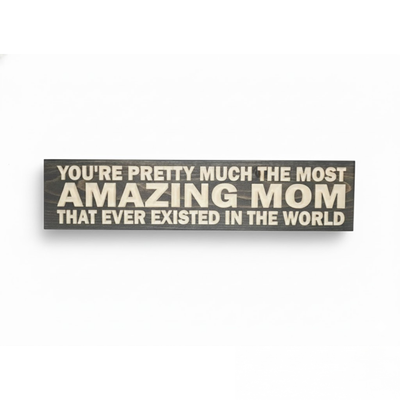 Flat lay view of a grey stained solid wood sign with "Most Amazing Mom" CNC-carved lettering.
