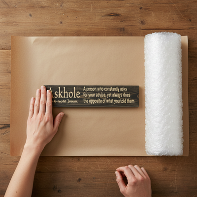 Preparing a handcrafted Askhole definition wood sign for shipping with protective bubble wrap.