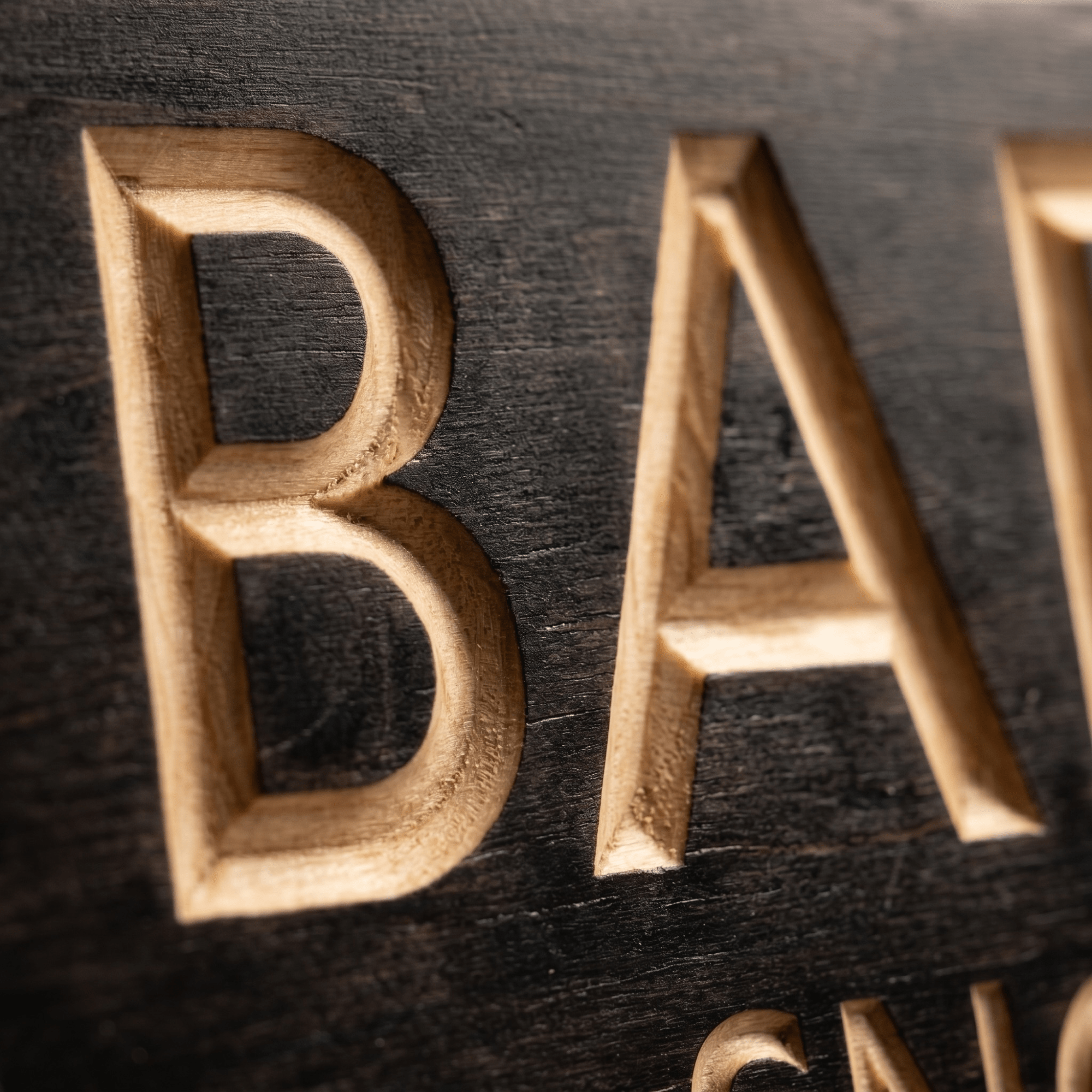 Macro close-up of CNC-carved letters revealing natural wood beneath the ebony stain.