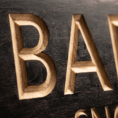 Macro close-up of CNC-carved letters revealing natural wood beneath the ebony stain.