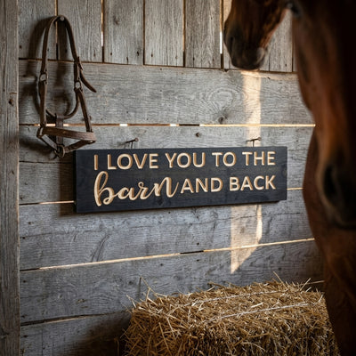 A black Barn Sign with "I LOVE YOU TO THE barn AND BACK" carved in light wood, hanging on a rustic barn wall with a horse, from Bluegrass Gifts