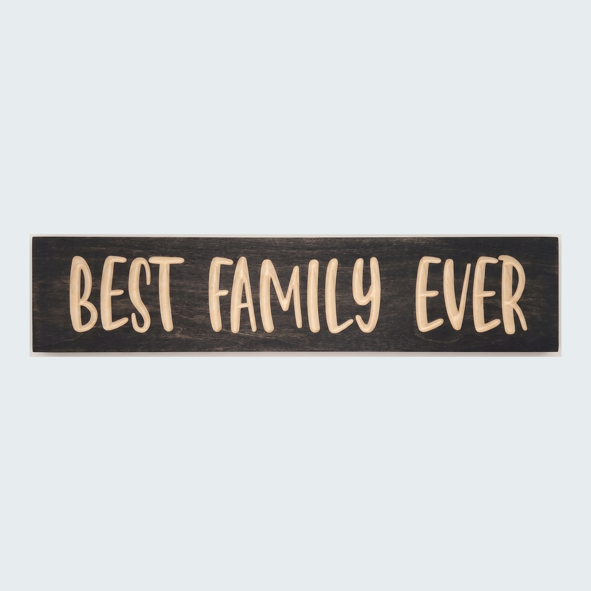 The Best Family Ever Sign, a dark wood plank with light carved letters, is centered on a plain gray background