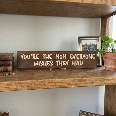 A carved Best Mom Sign sits on a wooden shelf next to old books and a framed family photo, from Bluegrass Gifts