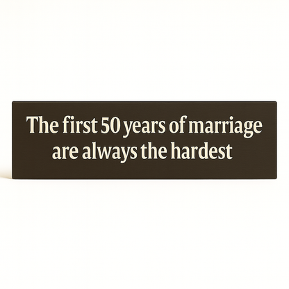 Straight-on studio shot of wooden anniversary sign that reads “The first 50 years of marriage are always the hardest.”