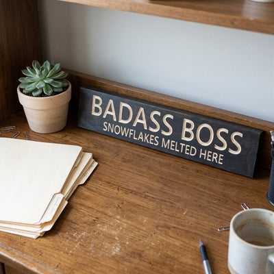 A dark wood Boss Lady Sign with light carved letters sits on a wooden desk next to a potted succulent and file folders from Bluegrass Gifts