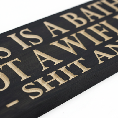 Close up view showing the 3D V-carve depth of the natural wood letters against the black stained surface of the Shit and Split sign.