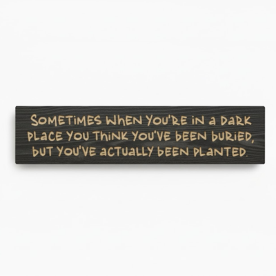 A high-quality product shot of the "Planted Not Buried" carved wood resilience sign in an ebony finish on a clean white background, showing the full inspirational quote.