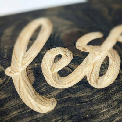 Close-up macro shot showing the deep CNC V-carved lettering and natural grain texture on the wood sign.