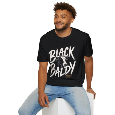 A man sitting comfortably on a white cube, modeling the black Cattle Shirt - Black Baldy with its full design