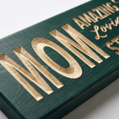"Close-up detail of the deep CNC carving on the 'MOM' wood sign by Bluegrass Gifts, highlighting the natural wood grain texture and teal finish."