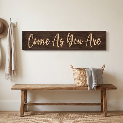 The Come As You Are sign hanging above a wooden entryway bench with a woven basket