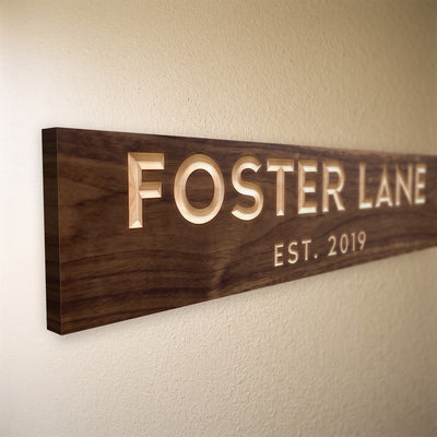 Close-up of the carved letters on the Foster Lane sign, natural pine inside the cuts against the stained grain