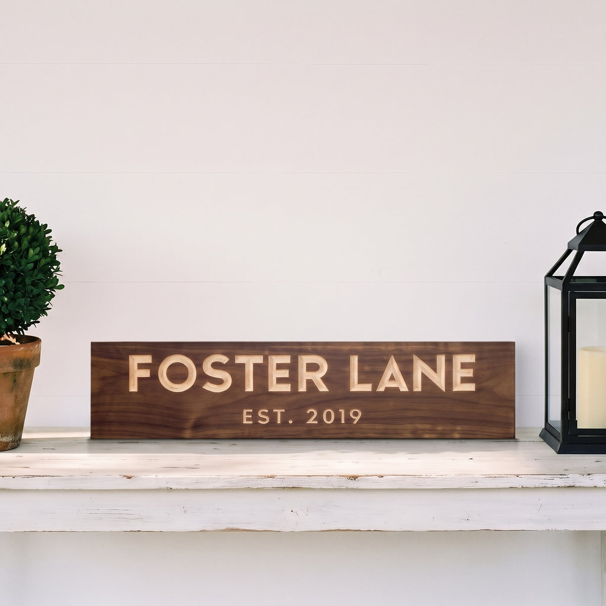 Foster Lane personalized wood sign standing on a white porch console table beside a boxwood topiary and a black lantern