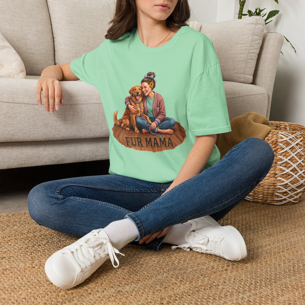 A woman sitting cross-legged on a woven rug, wearing a light green Dog Mom Shirt - Fur Mama, with a sofa behind her