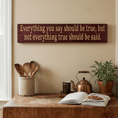 Everything You Say Should Be True truth quote wood sign hanging above a vintage kitchen sideboard with brass kettle, wooden utensils, sage plant, and open cookbook