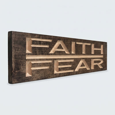 A side view of the Faith Over Fear Sign shows its dark stained wood and deeply carved, light-colored letters