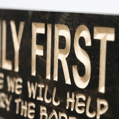 Close-up macro detail of CNC-carved Family First funny farmhouse sign showing dimensional wood lettering and natural grain on dark-stained solid Pine