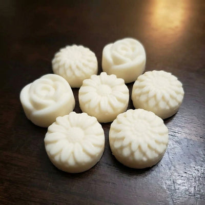 A small group of cream rose and daisy wax melts on a dark wood table