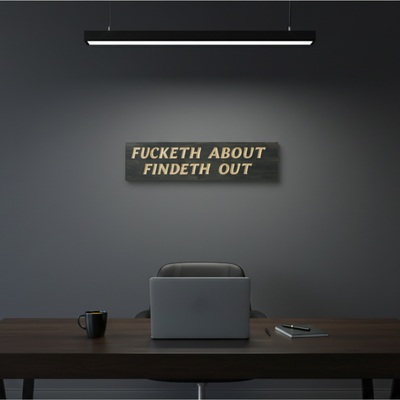  A "Fucketh About Findeth Out" sign on a minimalist desk in a home office with a laptop, showing it's for someone who values direct communication.