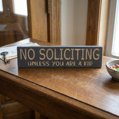 A No Soliciting Sign rests on a rustic wooden table next to a key and a small bowl of colorful candies, from Bluegrass Gifts
