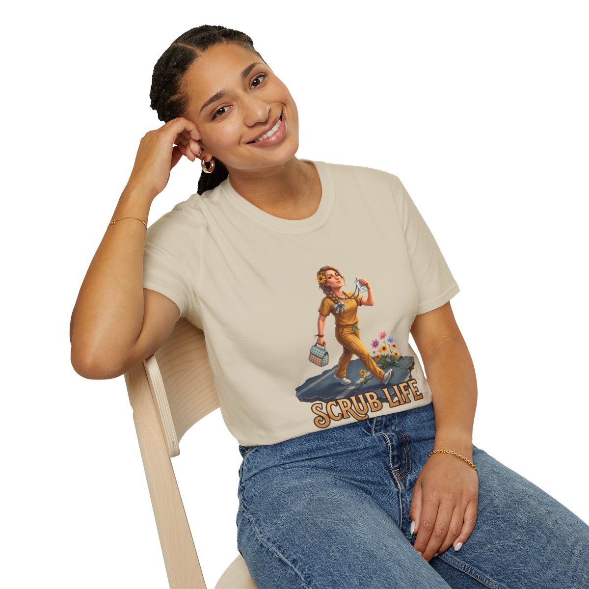 A woman with dark braided hair smiles, leaning on a chair, wearing a light beige "Nurse Shirt - Scrub Life" tee and blue jeans