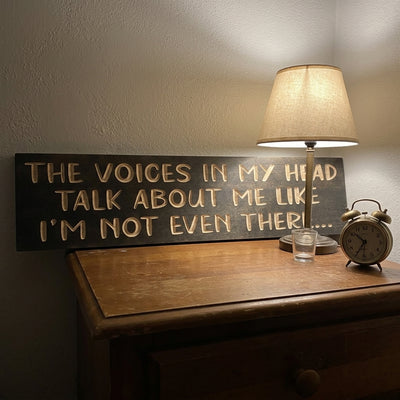 This dark, humorous Wooden Sign sits on a warm, lit nightstand next to a lamp and alarm clock, from Bluegrass Gifts