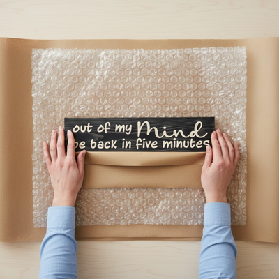 Overhead view of a Bluegrass Gifts sign being carefully hand-wrapped in kraft paper and bubble wrap for shipping.