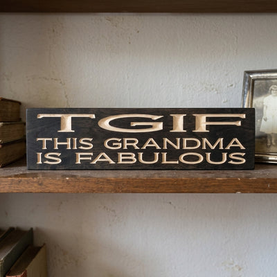 A close-up of a dark wood "TGIF: THIS GRANDMA IS FABULOUS" Grandma Sign on a rustic shelf from Bluegrass Gifts