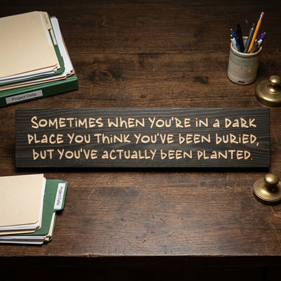 An overhead view of a dark wood Grit Sign on a rustic wooden desk with folders and a pen holder from Bluegrass Gifts