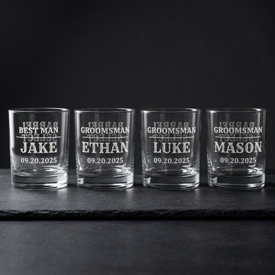 Four personalized groomsmen whiskey glasses on dark slate, Barrel Select engraving visible through the glass