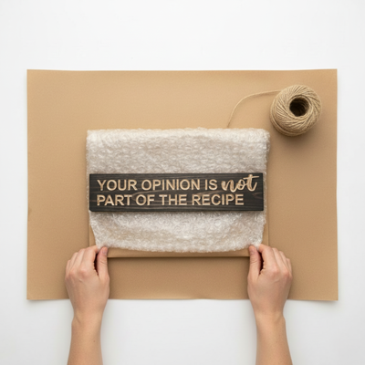 A Bluegrass Gifts wooden kitchen sign being carefully hand-wrapped in bubble wrap and kraft paper for shipping.