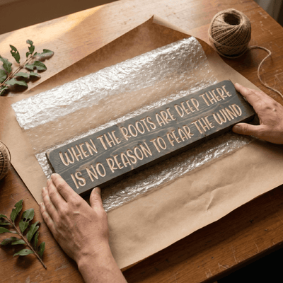 Hands wrapping a handmade When the Roots Are Deep inspirational wood sign in kraft paper at the Bluegrass Gifts workshop in Rineyville Kentucky