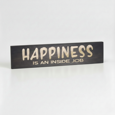 Close-up angled shot of the Happiness Is An Inside Job sign highlighting the 3D depth of the CNC V-carve lettering and solid wood texture.