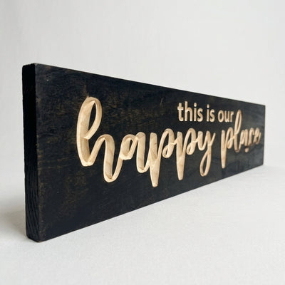 A side view of the black Camper Sign with light wood letters, showing its thickness and the carved text