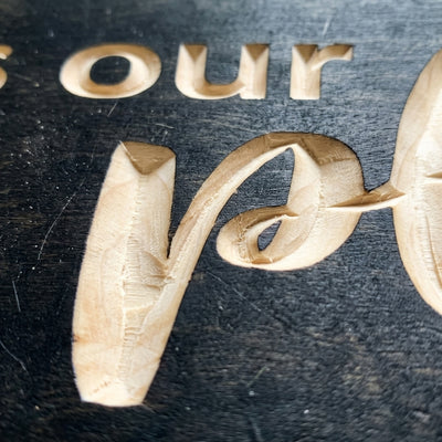 A close-up detail of the deeply carved "happy" letters on the dark wood Camper Sign, revealing the natural wood grain