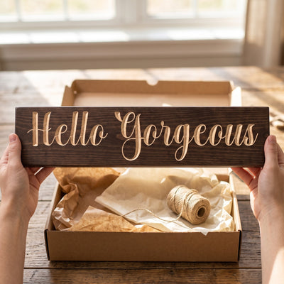 Hands holding the Hello Gorgeous sign over a kraft gift box with tissue paper