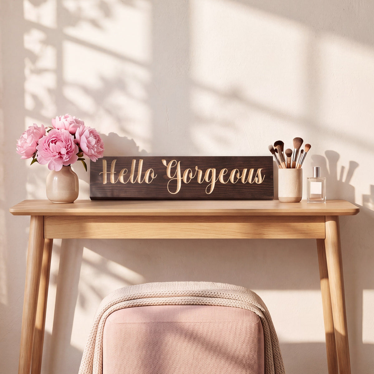 The Hello Gorgeous sign leaning on a white oak vanity table beside pink peonies and a cup of makeup brushes