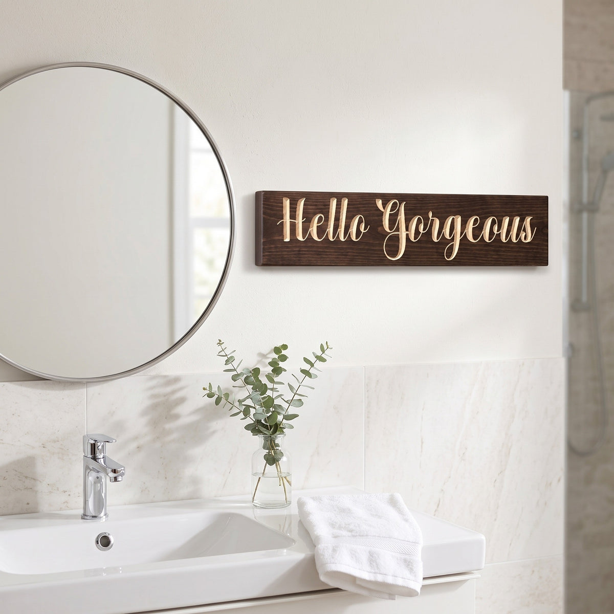 The Hello Gorgeous sign hanging beside a round mirror above a white bathroom vanity
