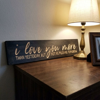 Angled view of the dark I Love You More Than Yesterday Sign on a wooden dresser, illuminated by a warm lamp from Bluegrass Gifts