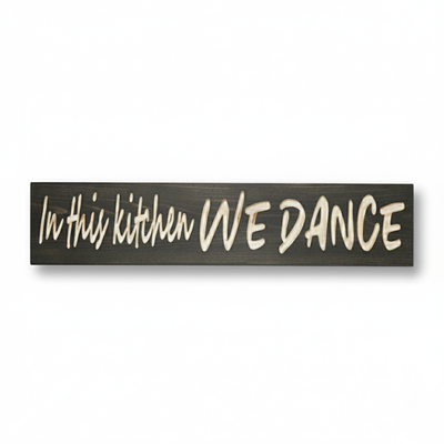 Front view of the "In This Kitchen We Dance" carved wood sign featuring a high-contrast dark walnut finish and natural wood grain lettering.