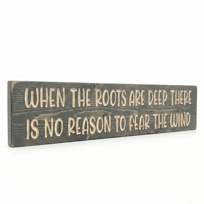 Angled view of solid pine When the Roots Are Deep wood sign showing dimensional CNC-carved lettering and weathered gray stain finish