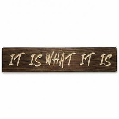 Isolated product shot of a dark walnut wooden sign with 'It Is What It Is' carved text on a clean white background.