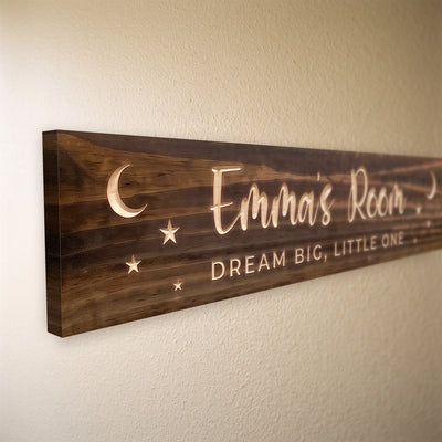 Close-up of the carved letters on the Emma's Room sign, natural pine inside the cuts against the stained grain