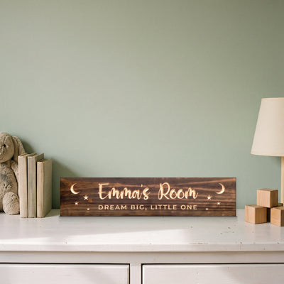 Emma's Room personalized wood sign standing on a white dresser beside a stuffed bunny, picture books, wooden blocks and a lamp