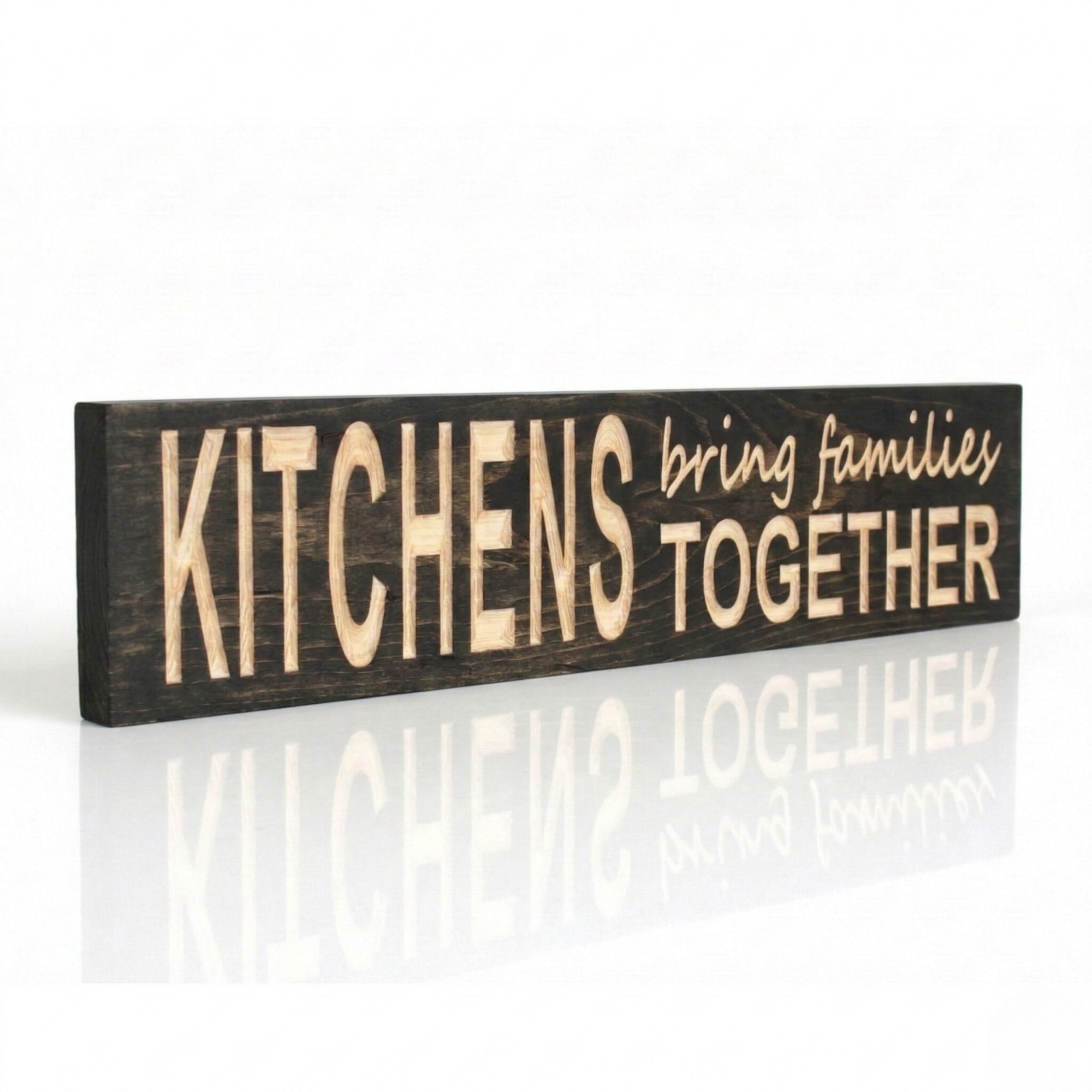 A side-view of a handcrafted dark wood sign by Bluegrass Gifts with CNC-carved lettering that reads "KITCHENS bring families TOGETHER" on a reflective white surface.