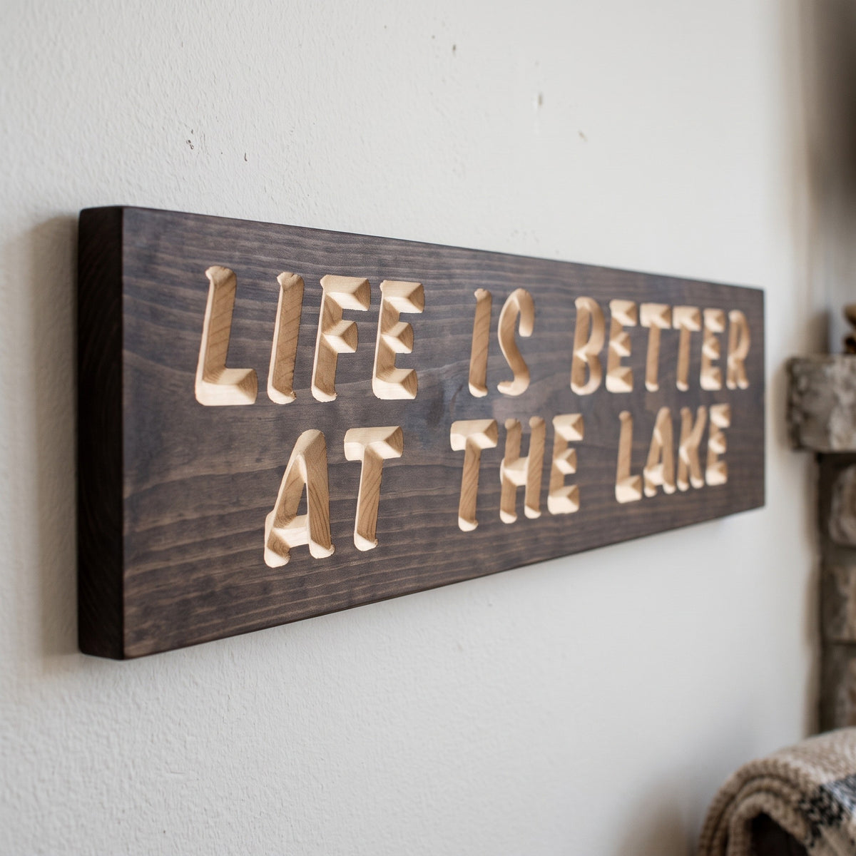 Close-up of the carved letters on the Life Is Better at the Lake sign, natural pine inside the cuts against the stained grain