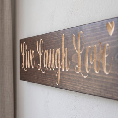 Close-up of the carved letters on the Live Laugh Love sign, natural pine inside the cuts against the stained grain