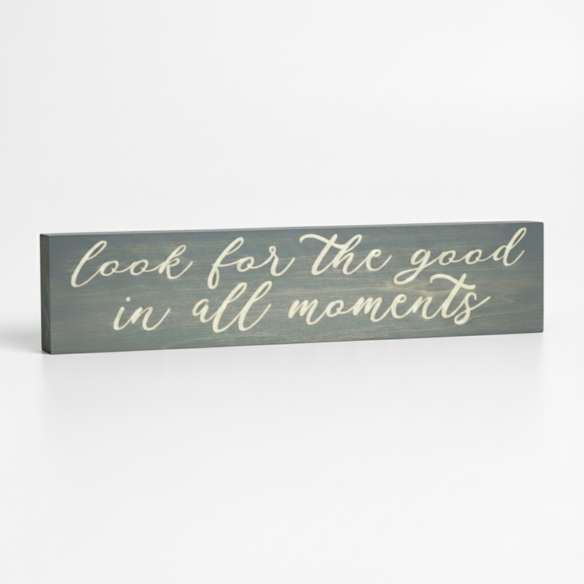 An angled view of the Bluegrass Gifts "Look for the good in all moments" carved wood sign displayed on a clean white surface.