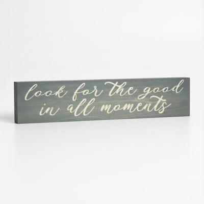 An angled view of the Bluegrass Gifts "Look for the good in all moments" carved wood sign displayed on a clean white surface.